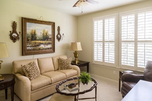 A beautifully furnished lounge space, featuring a brown leather sofa, wall décor, and timeless plantation shutters.