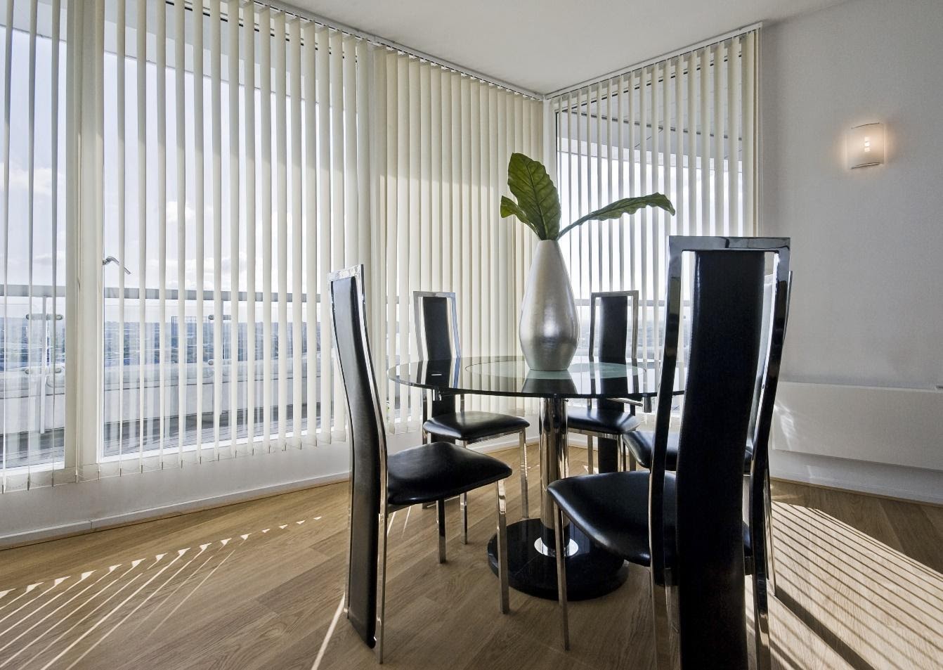 stylish modern dining room with a round glass top table and seats for five with vertical venetian blinds